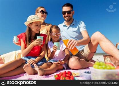 family, leisure and people concept - happy mother, father and two daughters having picnic on summer beach and drinking juice. happy family having picnic on summer beach