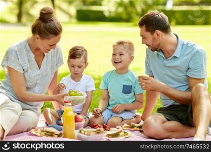 family, leisure and people concept - happy mother, father and two little sons having picnic at summer park. happy family having picnic at summer park