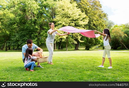 family, leisure and people concept - happy mother with daughter laying down picnic blanket on grass in summer park. family laying down picnic blanket in summer park