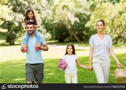 family, leisure and people concept - happy mother with picnic basket, father and two daughters walking in summer park. family with picnic basket walking in summer park