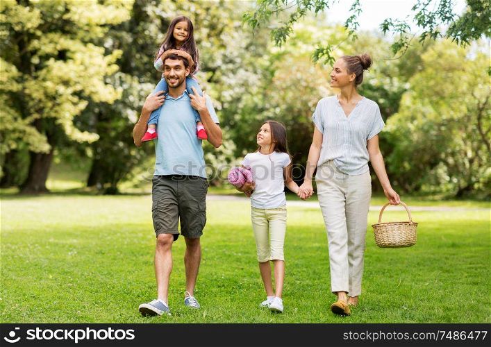 family, leisure and people concept - happy mother with picnic basket, father and two daughters walking in summer park. family with picnic basket walking in summer park