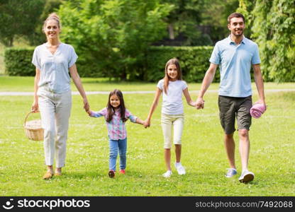 family, leisure and people concept - happy mother with picnic basket, father and two daughters walking in summer park. family with picnic basket walking in summer park