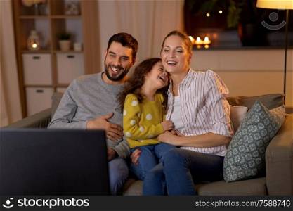 family, leisure and people concept - happy smiling father, mother and little daughter watching tv at home at night. happy family watching tv at home at night