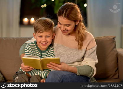 family, leisure and people concept - happy smiling mother and little son reading book sitting on sofa at home. happy mother and son reading book sofa at home