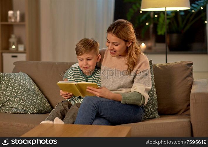 family, leisure and people concept - happy smiling mother and little son reading book sitting on sofa at home. happy mother and son reading book sofa at home
