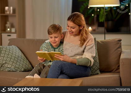 family, leisure and people concept - happy smiling mother and little son reading book sitting on sofa at home. happy mother and son reading book sofa at home