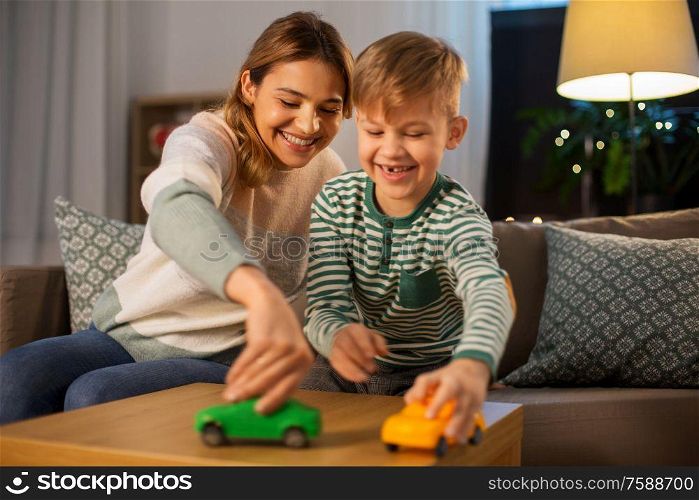 family, leisure and people concept - happy smiling mother and son playing with toy cars at home in evening. mother and son playing with toy cars at home