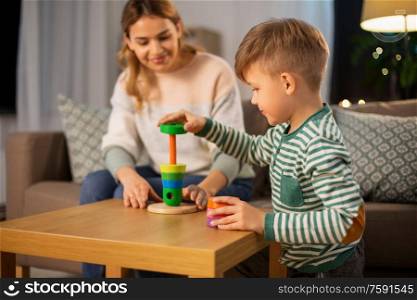 family, leisure and people concept - happy smiling mother and son playing with toy pyramid at home in evening. mother and son playing with toy pyramid at home