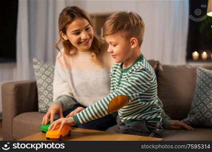 family, leisure and people concept - happy smiling mother and son playing with toy cars at home in evening. mother and son playing with toy cars at home