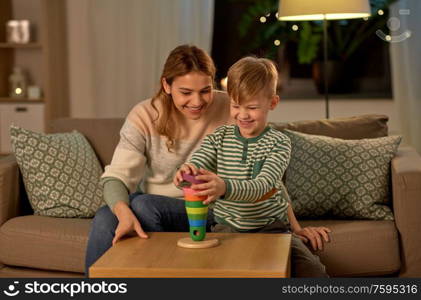 family, leisure and people concept - happy smiling mother and son playing with toy pyramid at home in evening. mother and son playing with toy pyramid at home