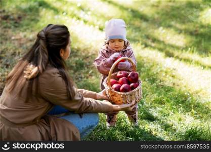 family, leisure and people concept - mother and baby daughter with apples in wicker basket at park. mother and baby daughter with basket of apples