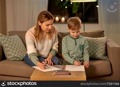 family, leisure and people concept - mother and little son with colored pencils and paper draw at home. mother and son with pencils drawing at home