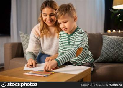 family, leisure and people concept - mother and little son with colored pencils and paper draw at home. mother and son with pencils drawing at home