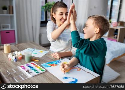 family, leisure and people concept - mother and little son with colors and paper drawing at home. mother and son with colors drawing at home
