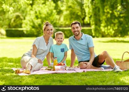 family, leisure and people concept - portrait of happy mother, father and little son having picnic at summer park. portrait of family having picnic at summer park