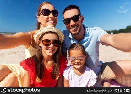 family, leisure and people concept - portrait of happy mother, father and two daughters in sunglasses taking selfie on summer beach. happy family in sunglasses taking selfie on beach