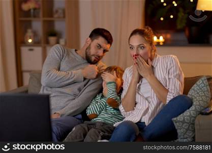 family, leisure and people concept - scared father, mother and little son watching tv at home at night. scared family watching tv at home at night
