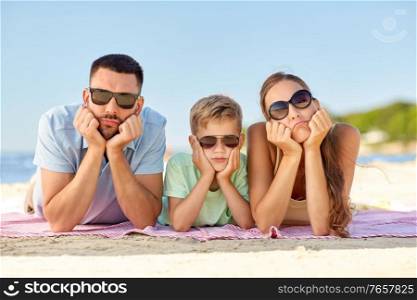 family, leisure and people concept - unhappy mother, father and little son in sunglasses lying on summer beach. unhappy family lying on summer beach