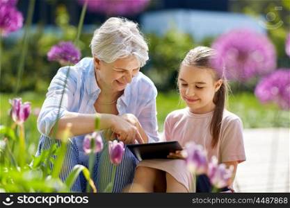 family, leisure and technology concept - happy grandmother and granddaughter with tablet pc computer at summer garden. grandmother and girl with tablet pc at garden. grandmother and girl with tablet pc at garden