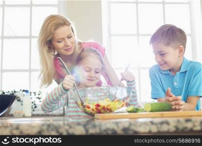 Family looking at girl mixing salad in kitchen