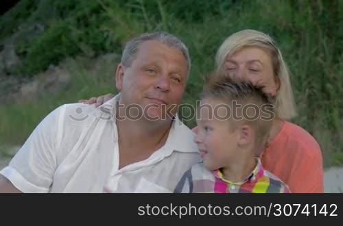 Family looking away. Grandson tickling grandfather&acute;s neck while sitting on beach