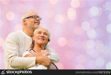 family, love, age and old people concept - happy senior couple hugging over pink holidays lights background