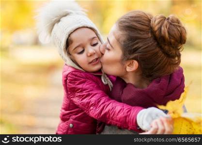 family, love and people concept - happy mother kissing her little daughter in autumn. mother kissing little daughter in autumn