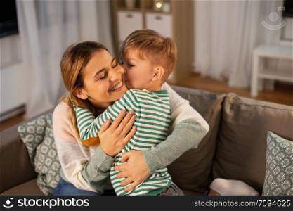 family, love and people concept - happy smiling mother and little son hugging and kissing at home in evening. happy mother and son hugging and kissing at home