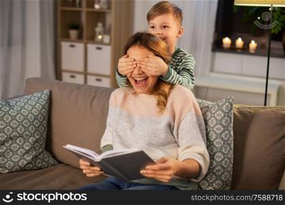 family, love and people concept - happy smiling mother with book playing game with her little son in evening. happy smiling mother playing with her son at home