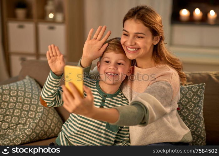 family, love and people concept - happy smiling mother with little son taking selfie by smartphone at home in evening. mother and son taking selfie by smartphone at home