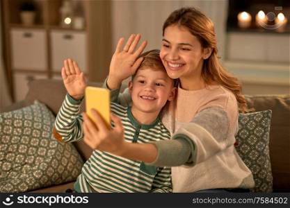 family, love and people concept - happy smiling mother with little son taking selfie by smartphone at home in evening. mother and son taking selfie by smartphone at home