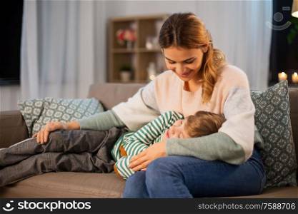 family, love and people concept - happy smiling mother with little son sleeping on sofa at home in evening. happy mother with sleeping little son at home