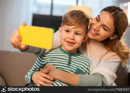 family, love and people concept - happy smiling mother with little son taking selfie by smartphone at home in evening. mother and son taking selfie by smartphone at home