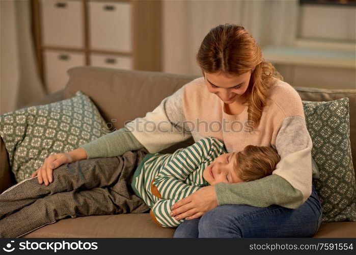 family, love and people concept - happy smiling mother with little son sleeping on sofa at home in evening. happy mother with sleeping little son at home