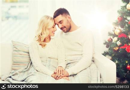 family, love, christmas, winter holidays and people concept - happy couple covered with plaid sitting on sofa at home. happy couple covered with plaid on sofa at home