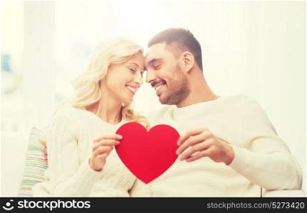 family, love, valentines day and people concept - happy couple with red heart hugging on sofa at home. happy couple with red heart hugging at home