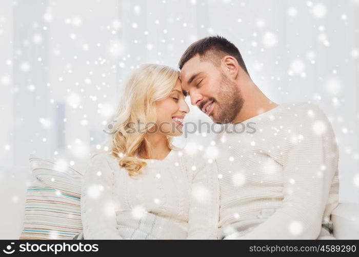 family, love, winter, holidays and people concept - happy couple covered with plaid sitting on sofa at home