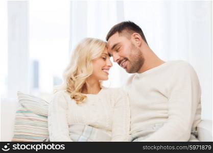 family, love, winter, holidays and people concept - happy couple covered with plaid sitting on sofa at home