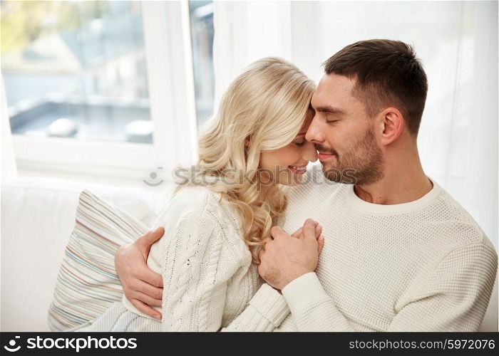 family, love, winter, holidays and people concept - happy couple covered with plaid sitting on sofa at home