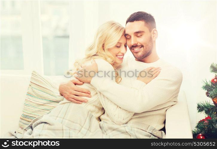 family, love, winter holidays, christmas and people concept - happy couple hugging on sofa at home. happy couple hugging on sofa at home