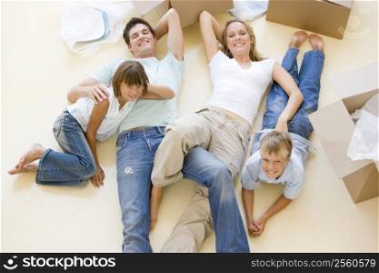 Family lying on floor by open boxes in new home smiling