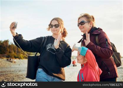 Family making gesture and waving during video call on smartphone during trip on summer vacation. Taking selfie photos
