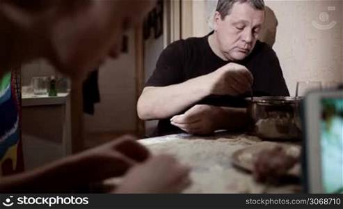 Family making pelmeni: one person giving dough, other man and woman stuffing them and talking