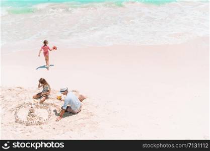 Family making sand castle at tropical white beach. Father and two girls playing with sand on tropical beach. Family making sand castle at tropical white beach.