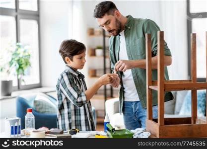 family, medicine and health concept - father healing son’s injured finger with antiseptic at home. father treats son’s injured finger with antiseptic