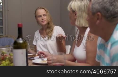 Family members are having dinner and holding a lively conversation, young blonde woman is gesturing actively.