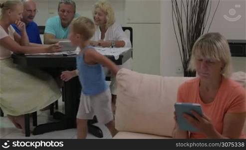 Family members busy with talks and tablet computers while child and grandmother playing tags