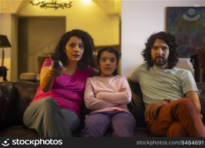 Family members watχng te≤vision whi≤sitting on sofa in living room