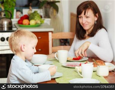 Family mother and blond son boy kid child eating corn flakes and bread breakfast morning meal at the table. Home.