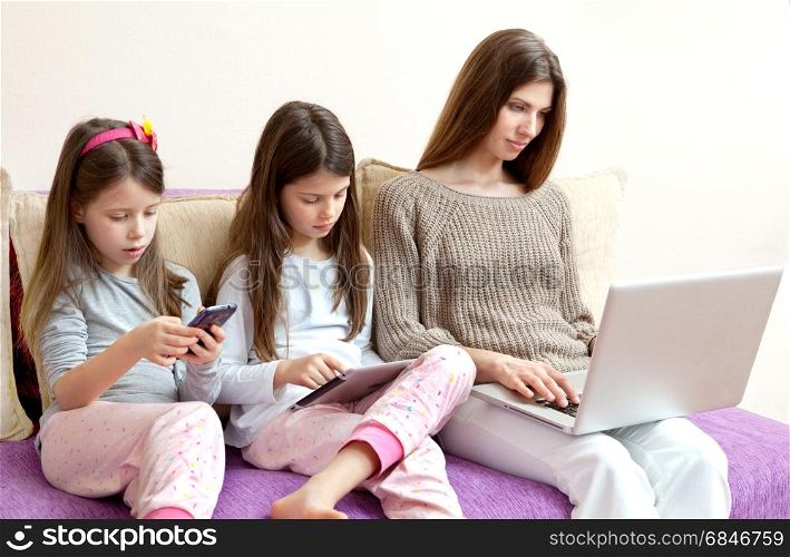 Family (mother and two daughters) watching phone and laptop (gadgets)